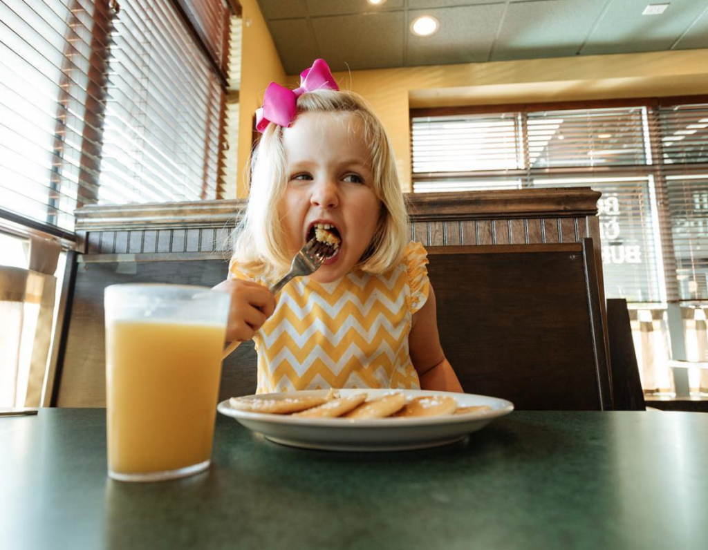 Little girl eating pancakes with a glass of orange juice