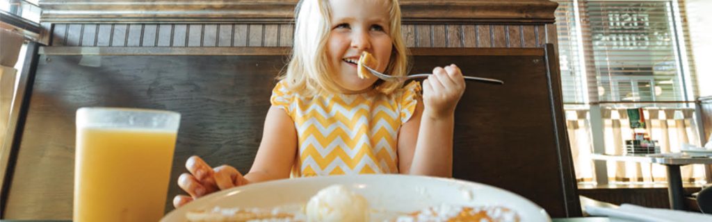 Girl eating pancakes with a glass of orange juice